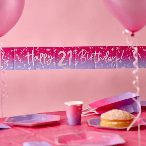 Happy 21st Birthday banner displayed above a pink party table with balloons, plates, cups, gift bags, and birthday decorations.
